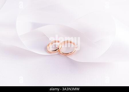 Elegante sfondo nuziale con due fedi nuziali dorate adagiate su un ampio nastro in raso bianco. Uno spazio di copia. cartolina. invito. Wedding Mockup for Design. Foto Stock