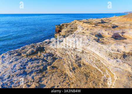 La vista panoramica cattura le aspre scogliere costiere di San Diego, mostrando rocce dorate che incontrano l'oceano blu profondo sotto un cielo limpido, ideale per il natur Foto Stock