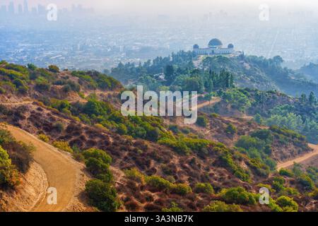 Vista panoramica dalle colline che si affacciano sull'Osservatorio Griffith e sulla città di Los Angeles, circondata da vegetazione e sentieri tortuosi, avvolta dalla foschia. Foto Stock