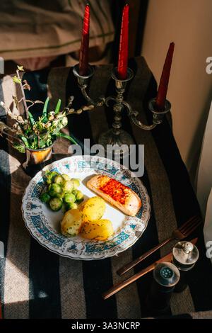Un delizioso piatto a base di salmone alla griglia, patate aromatizzate e cavolini freschi di bruxelles è ben disposto su un piatto a motivi geometrici. Le candele aggiungono il cha Foto Stock