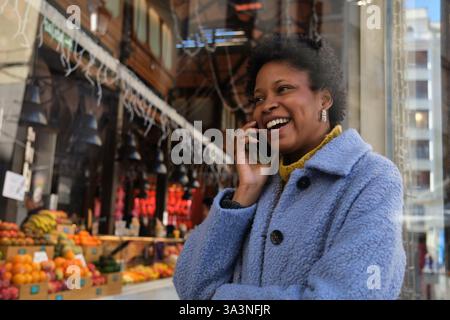 Cliente soddisfatto che effettua una telefonata vicino a un punto vendita di frutta fresca in un mercato Foto Stock