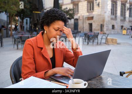 Donna stressata che ha mal di testa mentre lavora con un notebook in un bar all'aperto Foto Stock