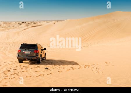 20 gennaio 2025, Abu Dhabi, Emirati Arabi Uniti: suv Toyota parcheggiato su dune di sabbia nel deserto durante un safari di una giornata di sole, circondato da tracce di pneumatici e impronte Foto Stock