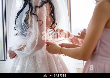 Una donna sta assistendo una sposa con i suoi preparativi per la bella e speciale occasione della sua cerimonia di nozze Foto Stock