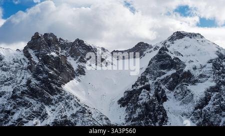 Snowy Mountain Peaks sotto un cielo parzialmente nuvoloso in inverno Foto Stock