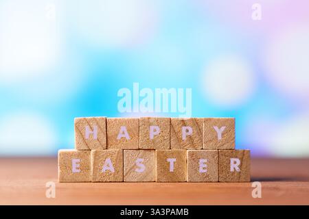 Blocchi di legno che spezzano FELICE PASQUA con uova di Pasqua colorate e fiori sullo sfondo sfocato. Una scena festosa e allegra che simboleggia la Pasqua Foto Stock