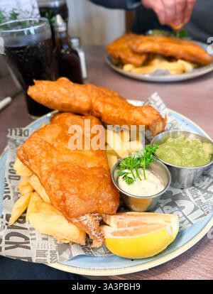 Un piatto di pesce e patatine fritte, servito con piselli moschi, salsa alla tartare e un spicchio di limone (erano deliziosi) Foto Stock
