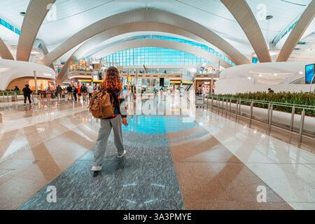 23 gennaio 2025, Abu Dhabi, Emirati Arabi Uniti: Donna viaggiatrice che cammina attraverso l'ampia sala di un moderno terminal aeroportuale Foto Stock