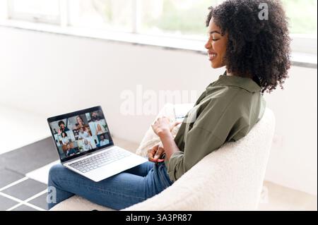 Seduto comodamente a casa, una giovane donna afroamericana si impegna in una conversazione ponderata durante un incontro online, mostrando un gesto di comprensione. Foto Stock