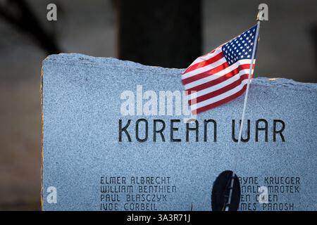 Una bandiera americana siede di fronte a un elenco dei morti della guerra di Corea al Manitowoc County Veterans Memorial Park di Manitowoc, Wisconsin. Foto Stock