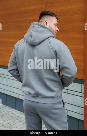 La parte posteriore di un uomo vestito con una comoda felpa con cappuccio grigia, dotata di tasca di canguro sul davanti Foto Stock