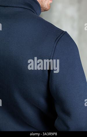 La vista si concentra sul retro di un uomo vestito con una felpa con cappuccio blu, che mostra vari stili nel tessile e nella moda Foto Stock