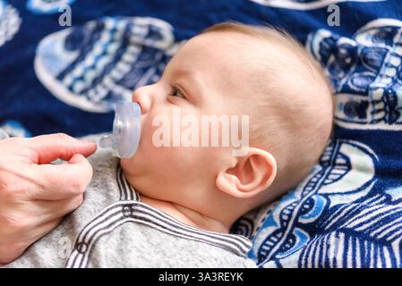 Bambino sdraiato su un letto con un succhietto Foto Stock