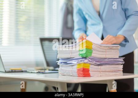 L'uomo d'affari che cerca importanti documenti contrattuali dalla pila di documenti sul tavolo conferma l'accordo che ha firmato con un investitore. Uomo d'affari chec Foto Stock