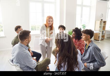 Gruppi diversi felici che parlano, condividono, tossicodipendenti seduti in cerchio su sedie durante una riunione di terapia di gruppo Foto Stock