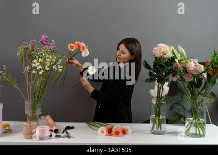 Creazione di composizioni floreali da gerberas per i clienti. Il fiorista sta sta raccogliendo fiori a margherita per bouquet in un negozio floreale Foto Stock