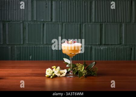 Provate il gusto raffinato di questo cocktail alla frutta della passione, presentato elegantemente in un bicchiere d'annata e decorato con fiori freschi. Perfetto per soph Foto Stock