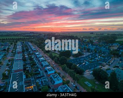 Vista aerea al tramonto di un quartiere periferico con cieli colorati, case moderne e dintorni verdi. I Paesi Bassi, Nijkerk. Foto Stock