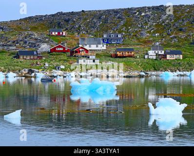 Vista panoramica di un piccolo villaggio di pescatori sulla costa rocciosa di un fiordo e di banchi di ghiaccio bluastro galleggianti nelle acque ghiacciate della Groenlandia occidentale. Danimarca Foto Stock
