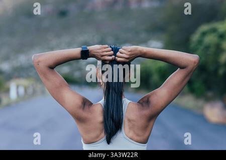 Vista posteriore di una donna sottile e irriconoscibile che regola i capelli mentre si sta in piedi all'aperto Foto Stock
