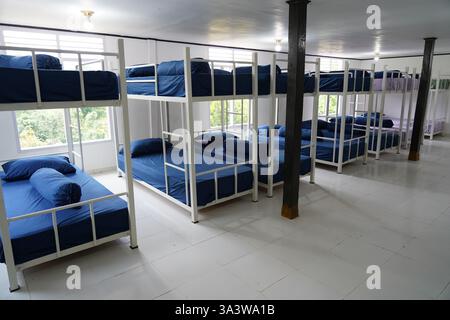 Una camera dormitorio ben organizzata con letti a castello in metallo bianco con biancheria blu, illuminazione naturale luminosa e un design minimalista pulito, id Foto Stock