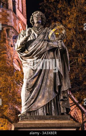 Sotto il soffice bagliore della notte, il monumento a Nicolaus Copernico si erge alto, celebrando l'eredità del famoso astronomo di Torun. Foto Stock