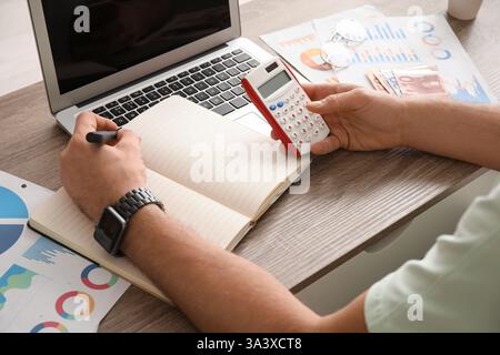 Mani maschili che scrivono qualcosa e fanno calcoli in ufficio. Primo piano Foto Stock