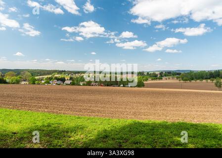 Campagna collinare con campi, piccolo villaggio di Wernitzgrun, prati e colline inferiori ricoperte da foreste nella regione del Vogtland in Germania Foto Stock