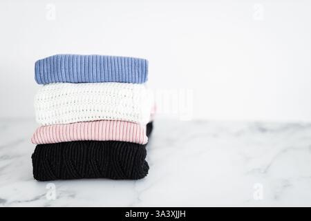 pile di maglioni e maglie in tessuto di diversi colori piegati e impilati con cura su sfondo minimalista Foto Stock