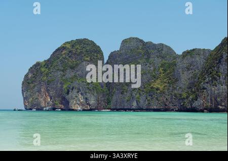 Le scogliere calcaree frastagliate sorgono dalle acque turchesi di Maya Bay, mentre le barche si radunano vicino alla riva di questo iconico paradiso tropicale Foto Stock