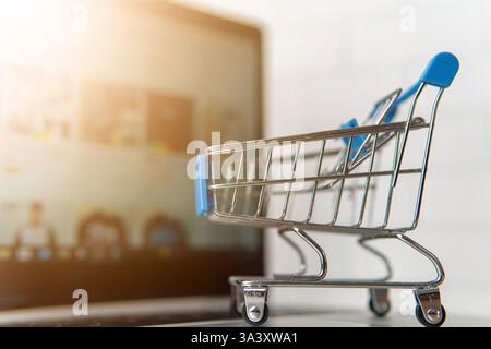 Un carrello con uno schermo sfocato del notebook sullo sfondo. Shopping online, concetto di e-commerce. Foto Stock