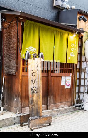 Ristorante tipico Giapponese a Dotonbori. Porta scorrevole in legno con tenda noren in consegna. Sul marciapiede cartello con menu in legno con luci attaccate. Foto Stock