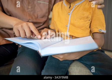 Ritratto di un padre musulmano indonesiano che insegna a suo figlio a leggere il corano. In attesa di tempo per iftar. Concetto di Happy Lebaran, Eid al Fitr, Idul Fit Foto Stock