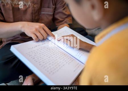 Ritratto di un padre musulmano indonesiano che insegna a suo figlio a leggere il corano. In attesa di tempo per iftar. Concetto di Happy Lebaran, Eid al Fitr, Idul Fit Foto Stock
