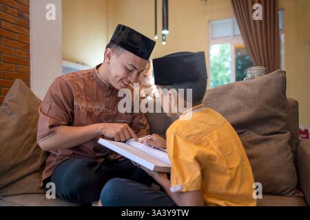 Ritratto di un padre musulmano indonesiano che insegna a suo figlio a leggere il corano. In attesa di tempo per iftar. Concetto di Happy Lebaran, Eid al Fitr, Idul Fit Foto Stock