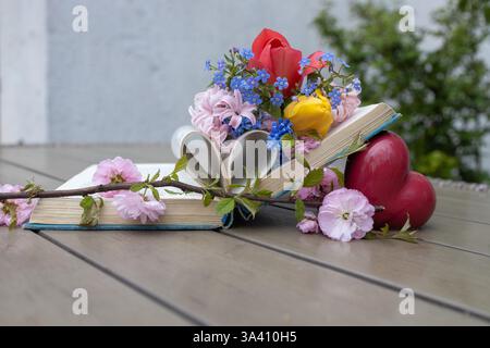 un vecchio libro spesso giace sul tavolo, tra le pagine ci sono molti fiori primaverili diversi, le pagine sono piegate a forma di cuore. Leggi il libro con piacere e un Foto Stock