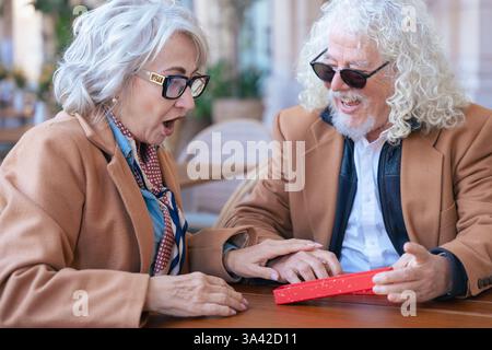 Felice coppia senior caucasica che si scambia un regalo in un caffè all'aperto momento gioioso. Foto Stock