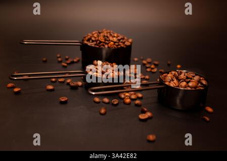 chicchi di caffè tostati in tazze graduate su uno sfondo scuro sparso sul tavolo Foto Stock
