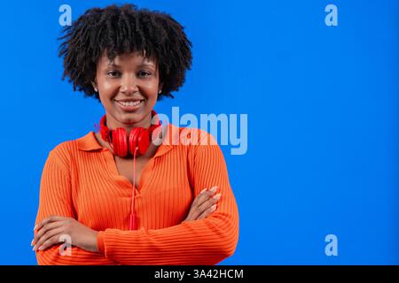 Donna afro-americana sorridente con cuffie rosse in posa su sfondo blu Foto Stock