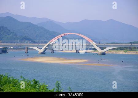 Gwangyang, Corea del Sud - 3 ottobre 2021: Un moderno ponte ferroviario con un caratteristico design ad arco attraversa il fiume Seomjin, con sponde di sabbia visibili Foto Stock