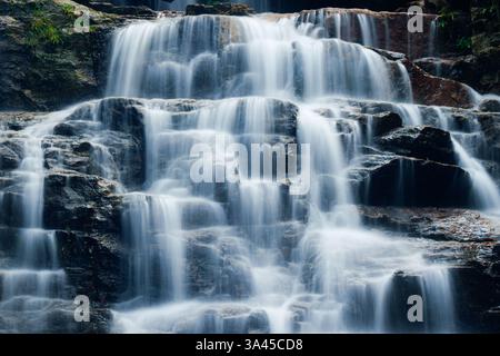 Splendida cascata che si estende su terreni rocciosi nella foresta tropicale, circondata da una vibrante vegetazione verde a Hoang su Phi, Vietnam Foto Stock