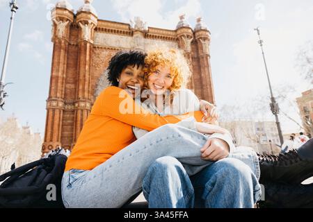 Due donne felici che abbracciano di fronte all'Arc de triomf a barcellona, spagna, godendosi la loro vacanza insieme Foto Stock