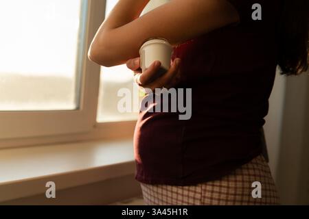 Primo piano di una donna in piedi accanto a una finestra che fissa un monitoraggio continuo del glucosio sul braccio Foto Stock