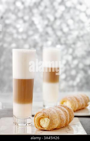 Due caffè latte macchiato con pasticcini ripieni di panna su un tavolo Foto Stock