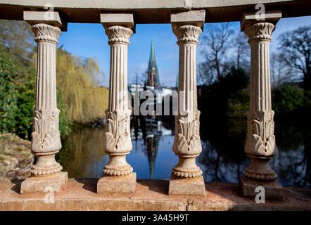 Oldenburg, Germania. 13 marzo 2025. Con il sole, la chiesa dei Lamberti si riflette dietro una storica balaustra nel laghetto con giardino del castello. La balaustra dal design elaborato è una caratteristica del parco storico. Crediti: Hauke-Christian Dittrich/dpa/Alamy Live News Foto Stock