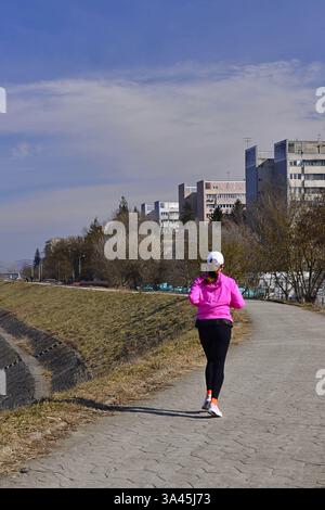 Donna solitaria in maglione rosa che corre sulle rive del fiume Mures Foto Stock
