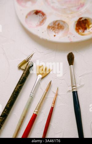 I pennelli e gli strumenti sono organizzati in modo ordinato, preparandosi per la creazione artistica su uno sfondo con texture chiare. Foto Stock