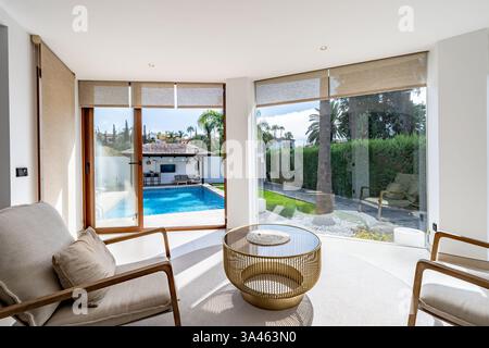 Un'immagine ravvicinata di un soggiorno con finestre di vetro che si affacciano sulla piscina privata nel giardino di lussuose ville mediterranee Foto Stock