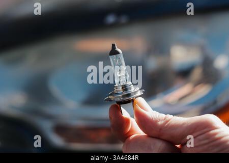 Primo piano di una lampada per auto in mano a un uomo sullo sfondo di un faro per auto. Foto Stock