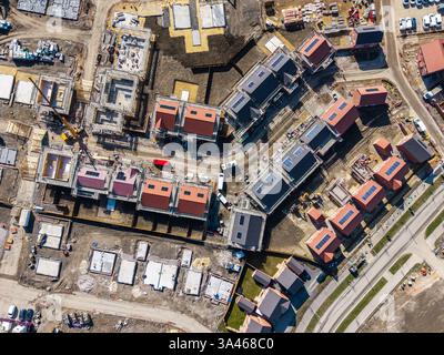 Vista aerea dall'alto verso il basso sopra un cantiere edile che costruisce nuove case ecologiche a prezzi accessibili con pannelli solari nel Regno Unito su un terreno con cintura verde Foto Stock